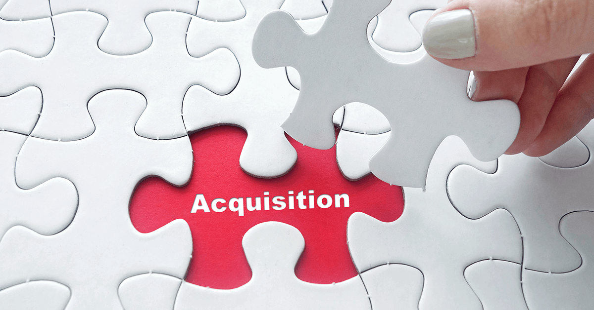 Closeup of a hand placing the final piece of a jigsaw puzzle with the word "acquisition."